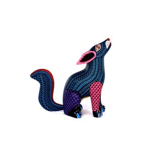 May include: A hand-painted wooden coyote figurine featuring a dark blue base color with intricate white dot patterns, pink ears, a purple checkered hind leg, and a pink checkered front leg, depicted in a seated position with its head tilted upward.