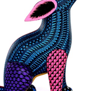 May include: A hand-painted wooden dog figurine featuring a dark blue base color with intricate light blue geometric patterns. The ears are bright pink with black centers, the front leg is pink with black triangles, and the back leg is purple with black squares.