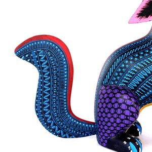 May include: A hand-painted wooden animal figurine featuring a curved tail with intricate blue and black geometric patterns and a red edge. The body displays a purple grid design on the haunches, while the black paws have blue accents.