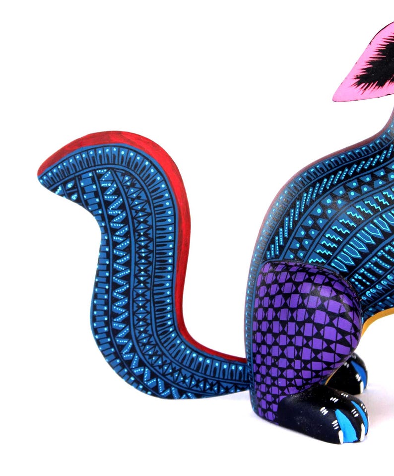 May include: A hand-painted wooden animal figurine featuring a curved tail with intricate blue and black geometric patterns and a red edge. The body displays a purple grid design on the haunches, while the black paws have blue accents.