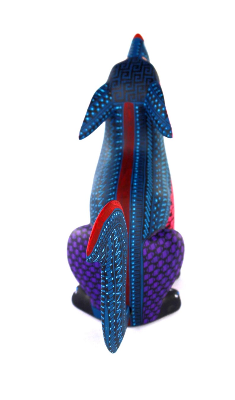 May include: A hand-painted wooden dog figurine featuring a vibrant blue base color with intricate black geometric patterns, purple textured hindquarters, and bright red accents on the ears, tail, and a central stripe along the back.
