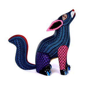 May include: A hand-painted wooden coyote figurine featuring a dark blue body covered in intricate light blue geometric patterns. The coyote has bright pink ears, a purple hind leg with a grid design, a pink front leg, and a curved tail.