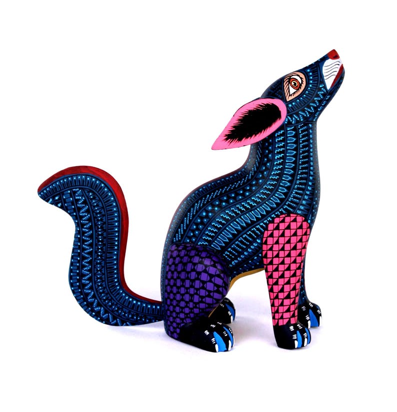 May include: A hand-painted wooden coyote figurine featuring a dark blue body covered in intricate light blue geometric patterns. The coyote has bright pink ears, a purple hind leg with a grid design, a pink front leg, and a curved tail.