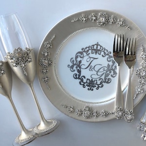 May include: Silver wedding cake serving set with two champagne flutes, a cake knife and two forks. The set is decorated with rhinestones and the plate has a monogram with the initials "J & G".