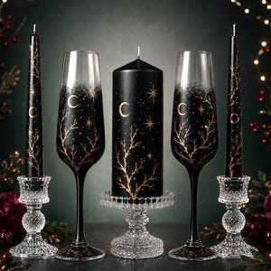 May include: Two black taper candles in clear crystal holders, two champagne flutes with black stems and gold celestial branch designs, and one central black pillar candle on a crystal pedestal, all featuring gold crescent moons and stars.