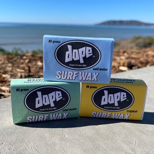 May include: Three bars of surfboard wax, each with the brand name "dope" and a different colour: blue, green, and yellow. The blue bar is labelled "cold water", the green bar is labelled "cool water", and the yellow bar is labelled "tropical".