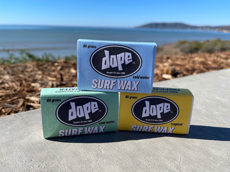 May include: Three bars of surfboard wax, each with the brand name "dope" and a different colour: blue, green, and yellow. The blue bar is labelled "cold water", the green bar is labelled "cool water", and the yellow bar is labelled "tropical".