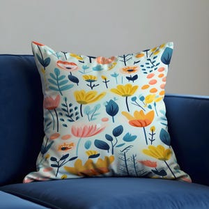 May include: A blue, yellow and pink floral patterned cushion with a white background. The cushion is sitting on a blue sofa.