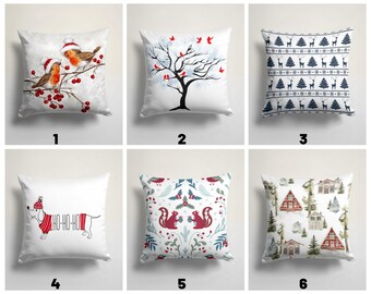 May include: Six different Christmas pillow designs. The first pillow features two red robins on a branch with red berries. The second pillow features a black silhouette of a tree with red birds. The third pillow features a blue and white pattern of reindeer and Christmas trees. The fourth pillow features a dachshund wearing a red and white Santa hat and a red and white striped sweater. The fifth pillow features a red squirrel and a red bird on a white background with green leaves and red berries. The sixth pillow features a white background with red and white houses and green trees.