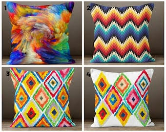 May include: Four colourful throw pillows with different geometric patterns. The pillows are arranged in a row on a wooden surface. The patterns include a swirling abstract design, a chevron pattern, and two different diamond patterns.