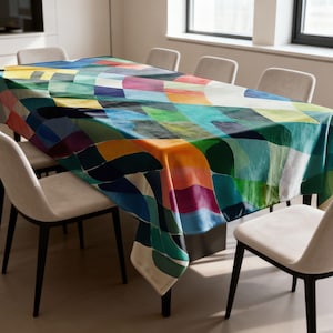 Peut inclure: Une nappe rectangulaire avec un motif abstrait coloré. Le motif présente des formes superposées dans des tons de bleu, vert, orange et violet. La nappe est drapée sur une table rectangulaire, entourée de chaises blanches.
