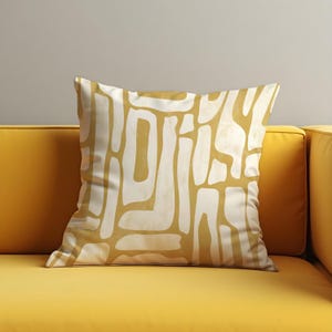 Può includere: Un cuscino giallo con un motivo geometrico astratto bianco. Il cuscino è su un divano giallo.
