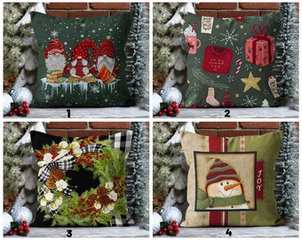 May include: Four different Christmas themed pillow covers. The first pillow cover features three gnomes wearing red hats and holding books. The second pillow cover features a green and red design with snowflakes, a candy cane, a mug, a sweater, and a gift box. The third pillow cover features a black and white checkered pattern with a green wreath, red berries, and white cotton balls. The fourth pillow cover features a snowman with a red hat and a green scarf, with the word "JOY" on the side.