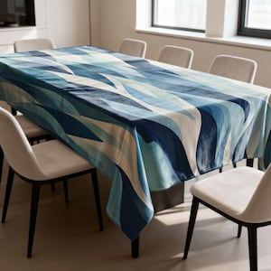 May include: A rectangular tablecloth with a blue and white wave pattern covers a dining table. The pattern features shades of blue and white in a flowing, abstract design. The table is surrounded by beige chairs.