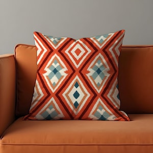 May include: Orange cushion with a geometric pattern in shades of red, white, blue, and orange. The pattern features a series of diamonds and stripes.