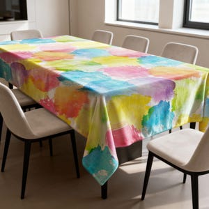May include: A rectangular tablecloth with a watercolor design. The pattern features large, overlapping brushstrokes in shades of yellow, pink, blue, purple, and orange. The tablecloth is draped over a dining table, with chairs surrounding it.