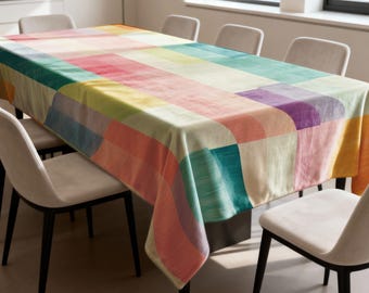 May include: A rectangular tablecloth with a colorful patchwork design. The pattern features large, irregular blocks of color in shades of pink, yellow, green, blue, and purple. The tablecloth is draped over a dark table, surrounded by light-colored chairs.