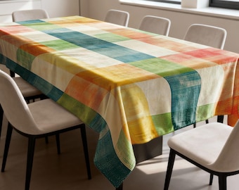 May include: A rectangular tablecloth with a colorful patchwork design. The pattern features squares and curved rectangles in shades of yellow, green, blue, orange, and red. The tablecloth is draped over a dining table, surrounded by chairs.