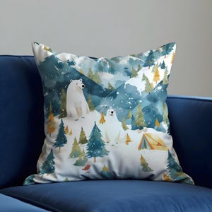 May include: A square cushion with a watercolour design of a snowy mountain scene. The design features two polar bears, evergreen trees, and a small tent. The colour palette includes shades of blue, green, white, and yellow.