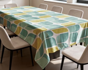 May include: A rectangular tablecloth with a repeating pattern of rounded rectangles in shades of yellow, teal, and light green on a white background. The tablecloth is draped over a dining table, with several chairs visible.