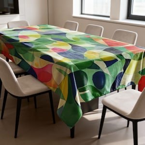 Peut inclure: Une nappe rectangulaire avec un motif abstrait coloré. Le motif présente des formes superposées dans des tons de vert, jaune, bleu, rouge et rose. La nappe est posée sur une table en bois, entourée de chaises blanches.