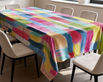 May include: A rectangular tablecloth with a vibrant, abstract design. The pattern features broad brushstrokes in shades of blue, yellow, pink, green, and orange. The tablecloth is draped over a wooden table, surrounded by neutral-toned chairs.
