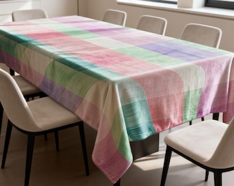 May include: A rectangular tablecloth with a colorful, geometric pattern. The design features large, curved rectangles in shades of pink, green, purple, and white. The tablecloth is draped over a dining table, surrounded by neutral-toned chairs.
