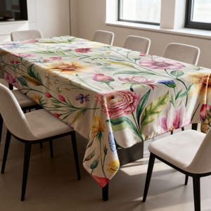 May include: A rectangular floral tablecloth featuring a watercolor design of colorful flowers, including pink, yellow, and blue blooms, on a cream background. The tablecloth is draped over a dining table with chairs.