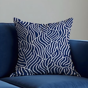 Puede incluir: Una almohada azul marino con un patrón abstracto blanco de líneas y curvas onduladas. La almohada está hecha de una tela suave y cómoda y es perfecta para agregar un toque de estilo a cualquier habitación.