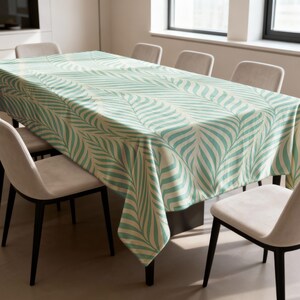 May include: A rectangular tablecloth featuring a teal palm leaf design on a cream backdrop. The cloth covers a dining table, surrounded by chairs. The pattern creates a fresh, modern look.