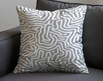 May include: Square throw pillow with a gray and white abstract pattern. The design features a series of interconnected, organic lines creating a maze-like appearance. The pillow is placed on a dark gray sofa.