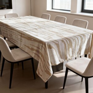 Puede incluir: Un mantel rectangular beige con un estampado de rayas de cebra cubre una mesa grande. La mesa está rodeada por ocho sillas beige con patas negras. La habitación tiene una paleta de colores neutros con luz natural.