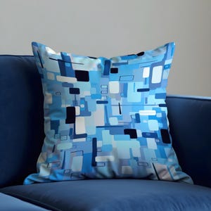 Peut inclure: Un coussin carré avec un motif géométrique dans les tons de bleu, blanc et noir. Le motif présente des formes rectangulaires et carrées disposées dans une composition abstraite. Le coussin est posé sur un canapé bleu.