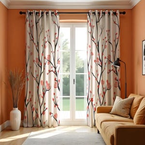 May include: Cream-colored window curtains with a black branch and red flower design. The curtains are hanging in front of a white window, with a tan couch and a black lamp in the room.