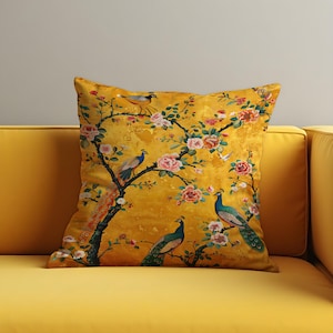 May include: A square cushion with a bright yellow backdrop. It displays a detailed print of peacocks on flowering branches with pink and red blooms. The cushion is placed on a yellow sofa.