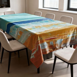 May include: A rectangular tablecloth with an abstract beach scene design. The top of the tablecloth features shades of blue and turquoise, transitioning to orange and yellow hues. The tablecloth is draped over a rectangular table, surrounded by beige chairs.