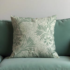 May include: A green and cream throw pillow with a floral pattern. The pillow is sitting on a green sofa.