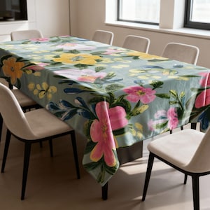 May include: A rectangular tablecloth with a floral pattern. The tablecloth features large pink, yellow, and orange flowers with green leaves on a light blue background. The tablecloth is on a rectangular table with six chairs.