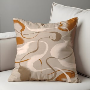 May include: A decorative throw pillow with an abstract design. The pillow features a beige background with flowing brushstrokes in shades of brown, white, and burnt orange. The pillow is square and rests on a white sofa.