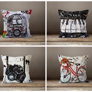 May include: Four decorative throw pillows with different designs. The pillows are made of white fabric with a variety of colorful images printed on them. The images include a vintage camera, a bicycle with flowers, a piano keyboard, and a building with a window.