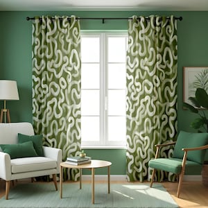 May include: A pair of green curtains with a white abstract pattern. The curtains are hanging in front of a window. A white armchair with green cushions, a small wooden table, and a green chair are in front of the curtains. The walls are painted green.