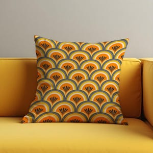 May include: Square decorative pillow with a retro fan pattern in shades of orange, yellow, gray, and white. The pillow is placed on a yellow sofa, creating a cohesive color scheme. The pillow's design is reminiscent of vintage art.