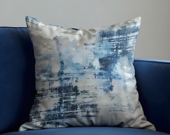 Può includere: Un cuscino decorativo quadrato con un design astratto nei toni del blu e del bianco. Il cuscino è posto su un divano blu. Il design presenta motivi simili a pennellate, creando un aspetto strutturato. Il tessuto del cuscino ha una lucentezza morbida e vellutata.