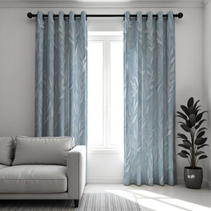Puede incluir: Cortinas azul claro con un diseño de hojas, colgadas de una barra negra. Las cortinas están junto a una ventana blanca y un sofá gris. Una planta en maceta está a la derecha de las cortinas.