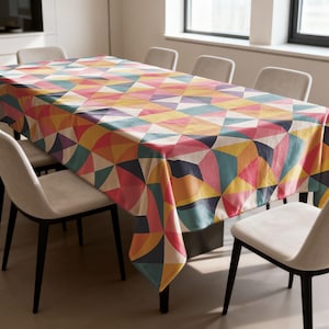 May include: A rectangular tablecloth featuring a geometric design in pink, yellow, orange, teal, and purple. The cloth covers a rectangular table, with chairs arranged around it.