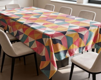 May include: A rectangular tablecloth with a geometric pattern in shades of pink, yellow, orange, teal, and purple. The tablecloth is draped over a rectangular table, surrounded by several chairs.