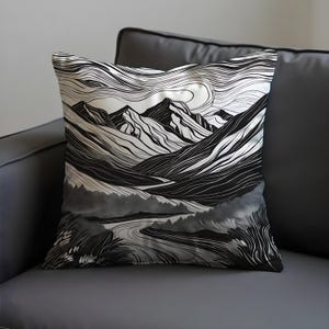 May include: Square throw pillow featuring a black and white mountain landscape design. The artwork depicts stylized mountains, a winding river, and swirling lines, creating a textured, artistic effect. The pillow is placed on a dark gray sofa.