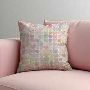 May include: Square decorative pillow with a pastel watercolor pattern of semi-circles in shades of pink, blue, yellow, and green. The pillow is placed on a pink sofa, creating a soft and inviting aesthetic. The pillow's design adds a touch of artistic flair to the room.