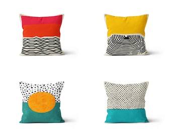 May include: Four decorative throw pillows with geometric patterns. The pillows feature black and white geometric designs, a yellow pillow with a black and white concentric circle design, and a teal pillow with a black and white polka dot design and a large orange circle.