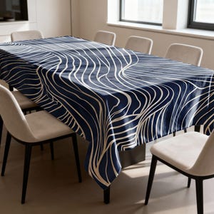 Puede incluir: Un mantel azul marino con un patrón abstracto ondulado de color crema. El mantel rectangular cubre una mesa de comedor, rodeada de sillas. El diseño le da al mantel un aspecto moderno.